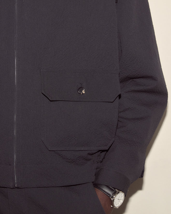Close-up of a person wearing the Seersucker Coach's Jacket in black, featuring a flap pocket, paired with a silver wristwatch.