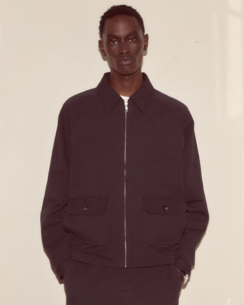 A person wearing the Seersucker Coach's Jacket stands against a plain, light-colored wall with hands in their pockets.