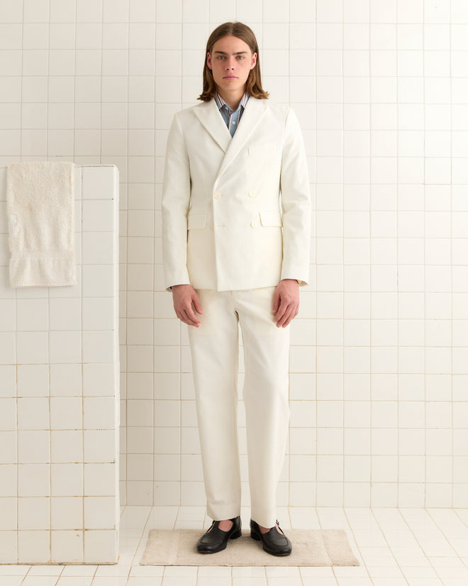 In a tiled room, a person stands in a crisp Seersucker Double-Breasted Suit Jacket, with gleaming buttons and a towel hanging on the wall.