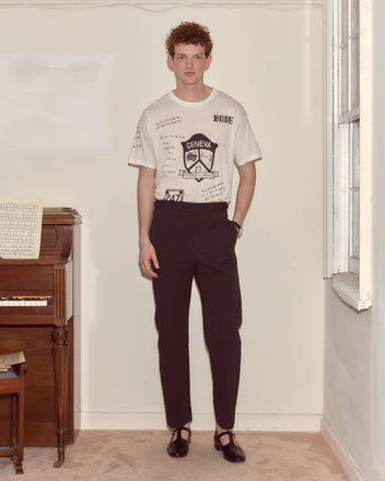 Person standing indoors by a piano, wearing a white graphic t-shirt, Seersucker Side Buckle Trousers - Dark Navy, and black shoes.