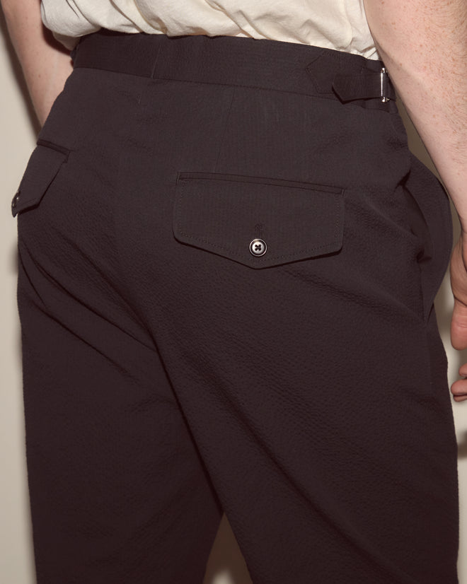 A person shown from behind wears Seersucker Side Buckle Trousers in dark navy with a buttoned back pocket and a white shirt.