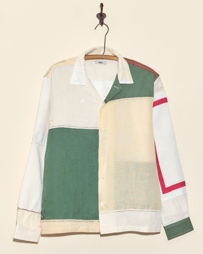 The Sandtree Napkin Shirt - L/XL features long sleeves and vintage patchwork panels in green, cream, white, and red. Displayed on a hook against a beige wall, it's truly one-of-a-kind.