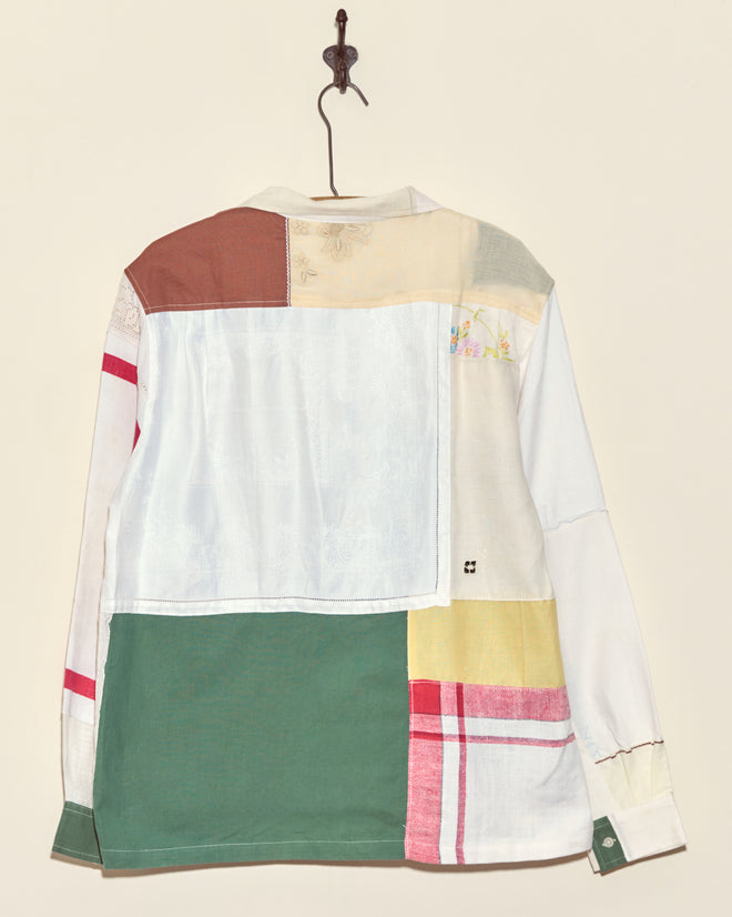 The Sandtree Napkin Shirt - L/XL features a unique patchwork of colorful fabric squares, evoking vintage napkin style, and is displayed hanging on a hook against a plain backdrop.