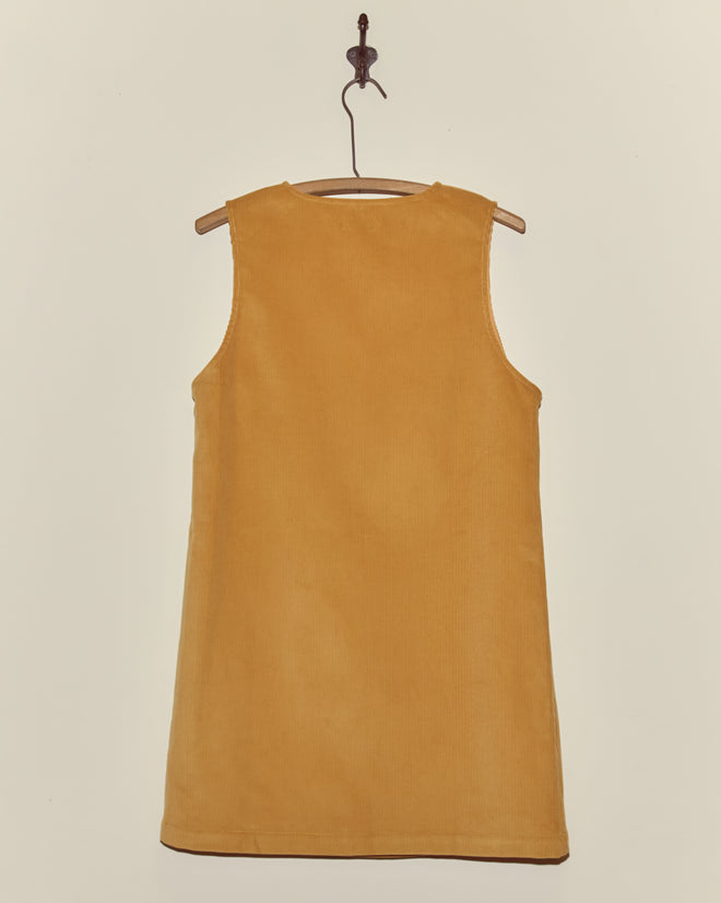 A Custom Senior Cord Dress in mustard yellow, inspired by classic British corduroy, hangs sleeveless on a wooden hanger against a plain light background.