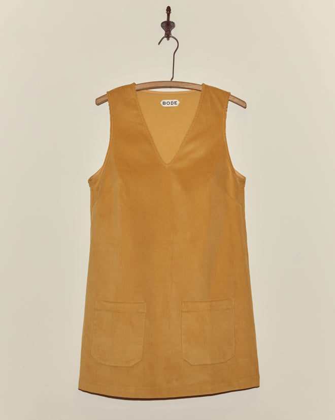 Custom Senior Cord Dress in sleeveless mustard yellow British corduroy, featuring two front pockets, displayed on a wooden hanger.