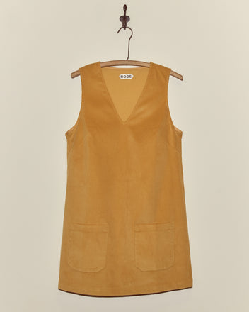 The Custom Senior Cord Dress is a sleeveless mustard yellow corduroy dress with two front pockets, displayed on a wooden hanger.