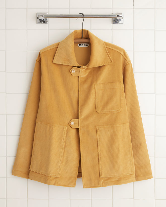 The Custom Senior Cord Front Tab Jacket, with its British design and spacious pockets, hangs elegantly on a tile wall, showcasing the timeless appeal of custom corduroy jackets.