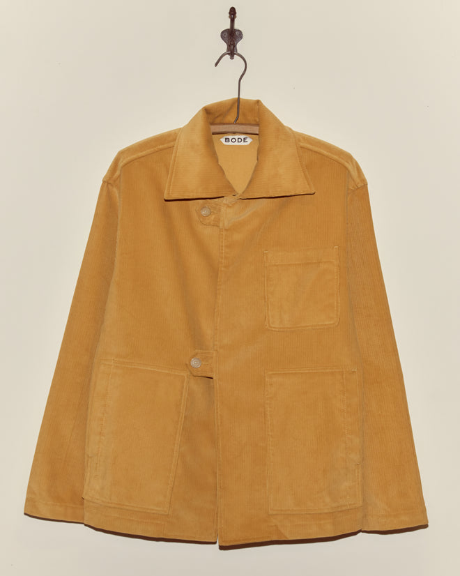 Custom Senior Cord Front Tab Jacket in light brown corduroy with three front pockets, displayed on a hanger against a beige wall—a classic piece inspired by collegiate styles.