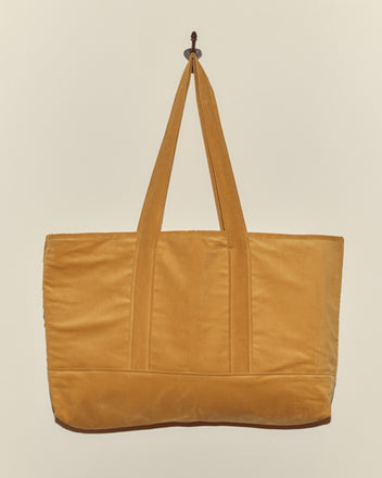 The Custom Large Senior Cord Tote in mustard yellow, with two handles, hangs on a hook against a light background—ideal for carrying your corduroy notebook or daily essentials.