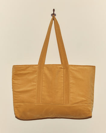 Custom Large Senior Cord Tote in yellow, featuring two handles and made from British corduroy, hangs on a wall hook against a plain beige background.