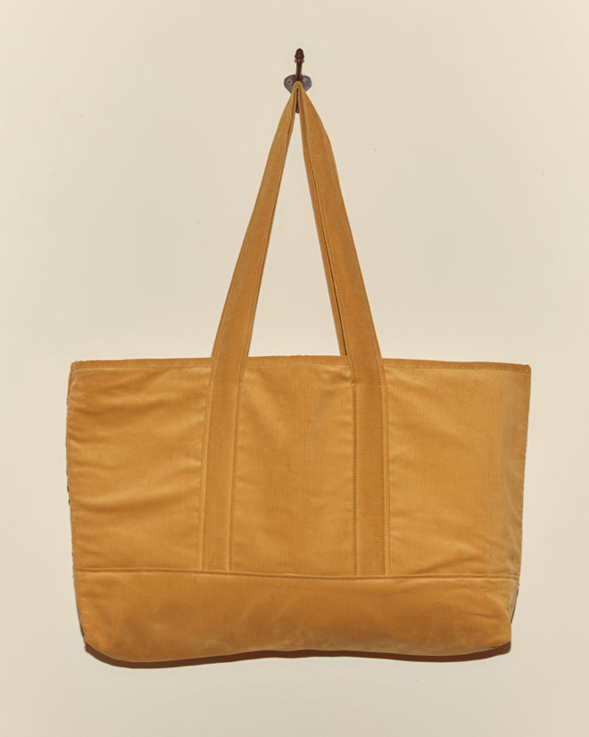 Custom Large Senior Cord Tote in yellow, featuring two handles and made from British corduroy, hangs on a wall hook against a plain beige background.