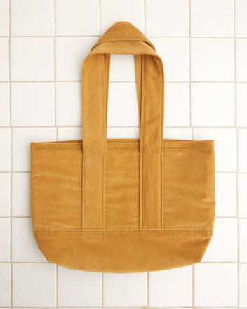 A Custom Small Senior Cord Tote in mustard yellow, made from British corduroy and featuring long handles, displayed against a white tile background.