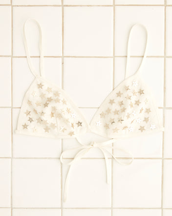 The Sequin Spangled Bra, an Indian-made white bralette, showcases sequined star patterns displayed on a tiled surface.