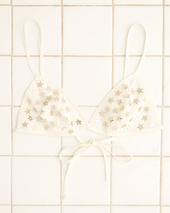 The Sequin Spangled Bra, an Indian-made white bralette, showcases sequined star patterns displayed on a tiled surface.