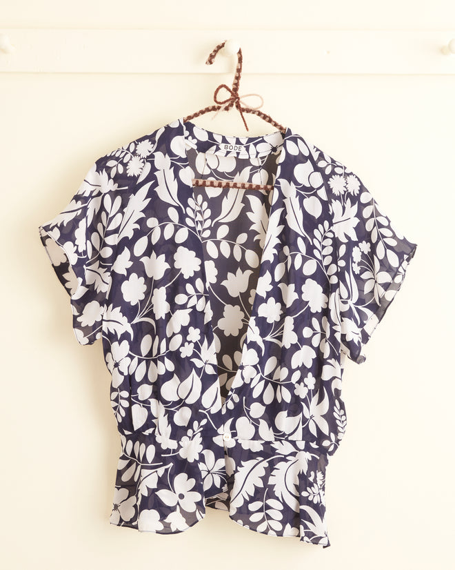 The Shadowed Ferns Top - 4, a floral black and white blouse made from deadstock dress fabric, hangs gracefully on a hanger against a pale background.