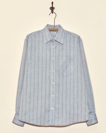 Shale Fletcher Shirt - M: Light blue long-sleeve button-up with subtle vertical stripes, crafted from deadstock shirting fabric, shown hanging on a hook.