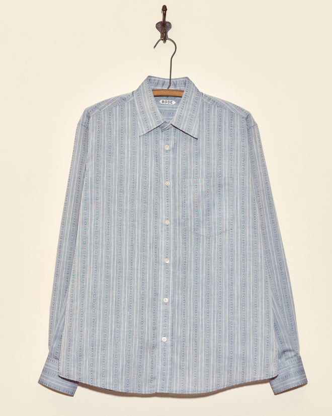 Shale Fletcher Shirt - M: Light blue long-sleeve button-up with subtle vertical stripes, crafted from deadstock shirting fabric, shown hanging on a hook.
