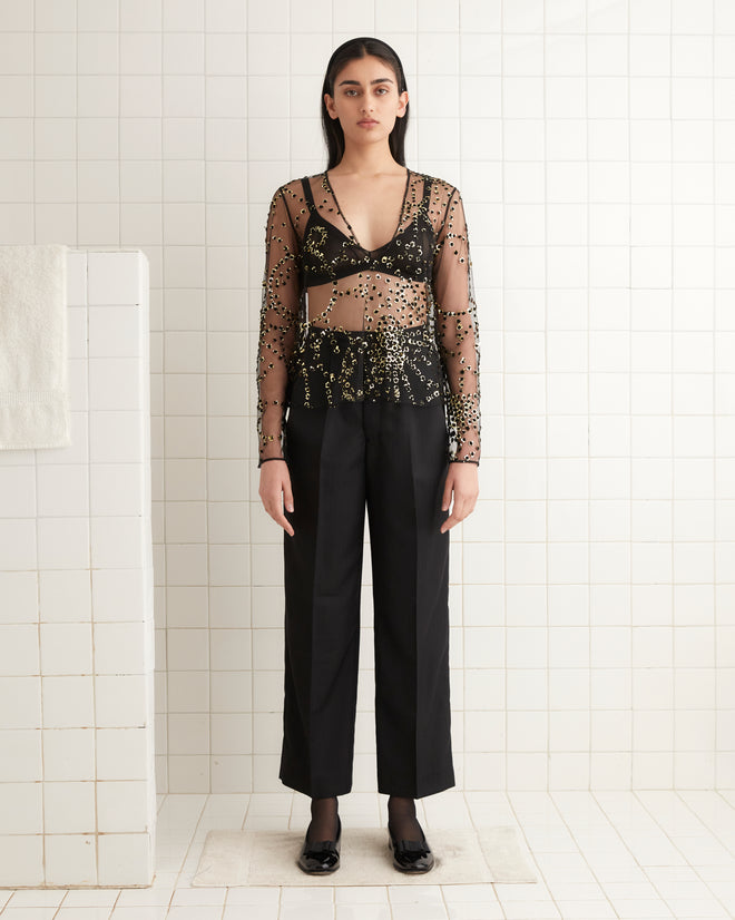 A person wearing the Sheer Fête Top and black pants stands against a tiled wall.