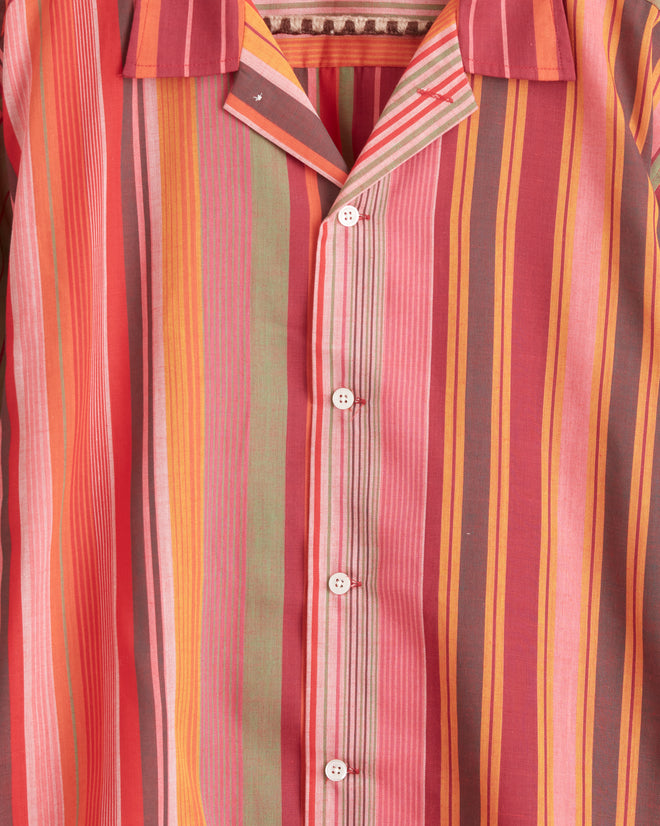 The Sherbet Stripe Shirt - XL/XXL, featuring a unique long-sleeved design with a vibrant stripe pattern, hangs on a hook against a light-colored wall.