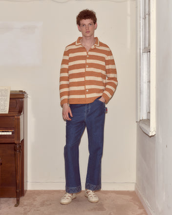 A person in a Sherbet Crochet Long Sleeve Shirt and blue jeans stands indoors near a piano and a bright window.