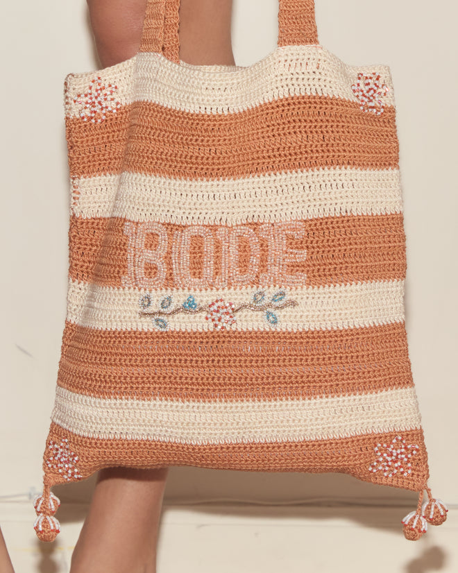 The Sherbet Crochet Tote is a beige and orange striped cotton bag with "BODE" and floral embroidery, shown being held by a person.