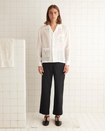 White linen long sleeve shirt featuring two pockets on the front with embroidered tumbling skiers.