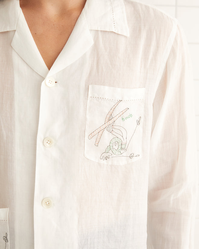 White linen long sleeve shirt featuring two pockets on the front with embroidered tumbling skiers.