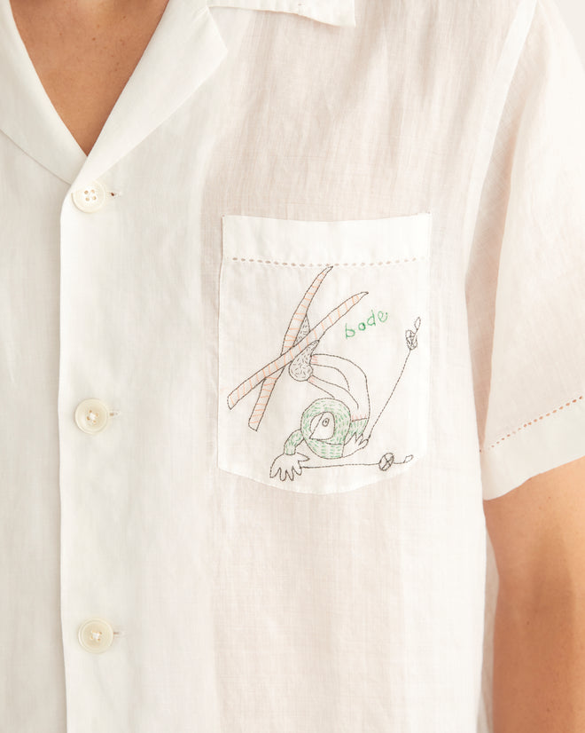 White linen short sleeve shirt featuring two pockets on the front with embroidered tumbling skiers.