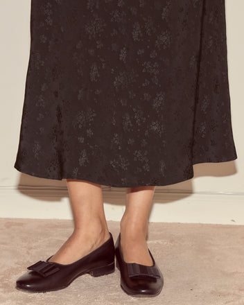 Wearing the Moonflower Jacquard Skirt in black and black bow loafers, a person stands on a beige carpet.