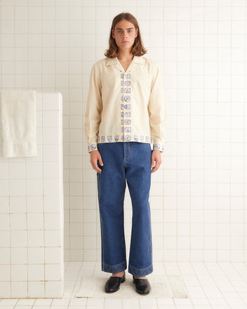 Cream silk shirt that features patterned crest down the front opening and bottom hem.