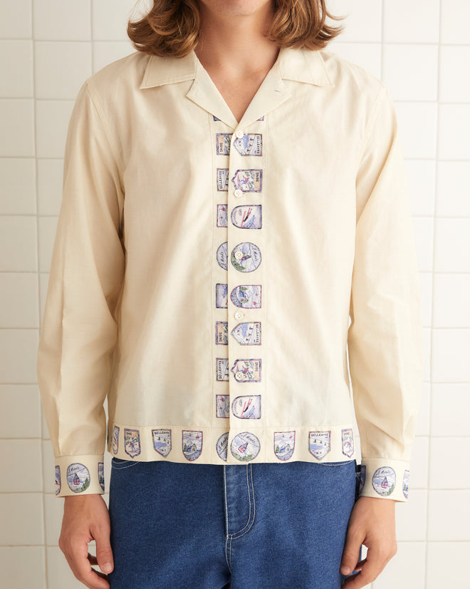 Cream silk shirt that features patterned crest down the front opening and bottom hem.