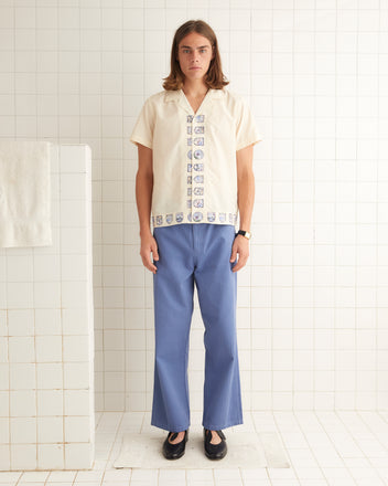 Cream silk shirt that features patterned crest down the front opening and bottom hem.