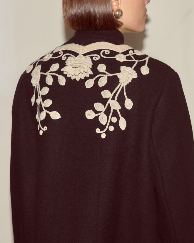 A woman with a sleek bob wears the Snowdrop Appliqué Jacket, a swing silhouette wool outerwear featuring white floral embroidery on the back.