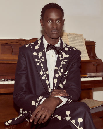 A person in a navy Snowdrop Appliqué Suit Jacket sits in front of a piano with sheet music.