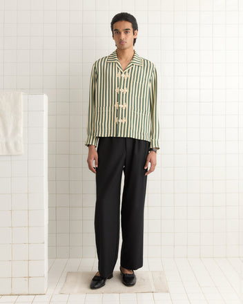 Someone wearing a Soda Stripe Trillium Shirt and black pants stands on a white tiled floor, with a towel draped over a nearby wall.