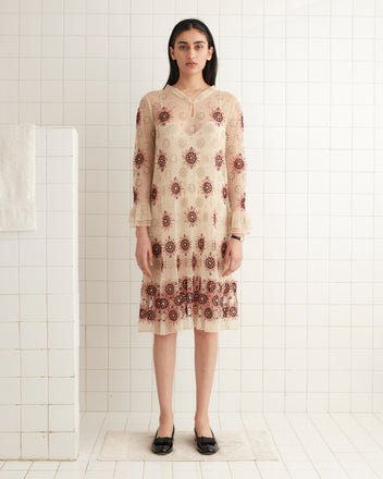 A woman in a vintage-inspired Solarium Dress stands gracefully in a tiled room, with a towel elegantly hanging on the nearby wall.