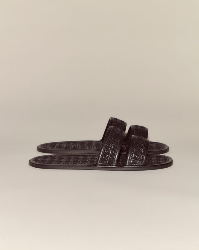 A pair of Solid Summer Slides in black, featuring textured straps and soles, is displayed on a plain beige background.