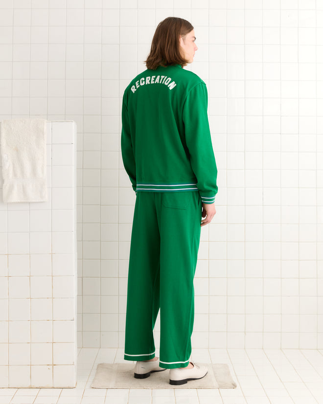 A person wearing the "Sophomore Jacket" stands in a tiled room with "RECREATION" on the back, showcasing their distinctive vintage jersey style. A white towel and floor mat subtly accentuate the scene.