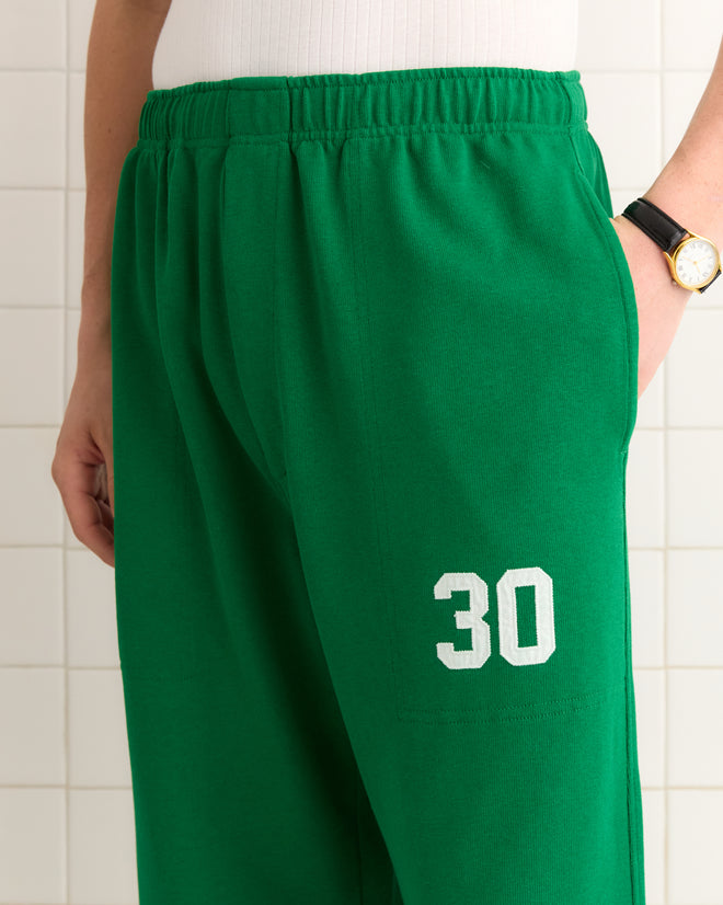 Someone is wearing Sophomore Sweatpants in green with the number 30, paired with a white shirt and a watch.