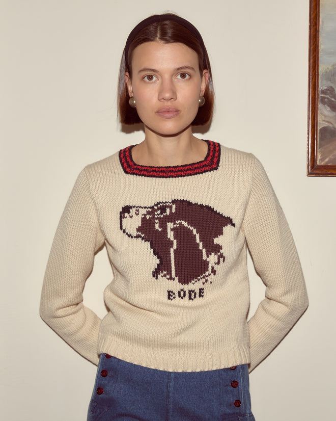 Woman in the Spaniel Sweater, a cream cotton merino blend featuring a bear graphic and "BODE" text, poses against a beige wall.