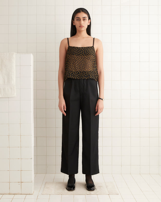 A woman wearing a sheer Stadium Dot Tank and black pants stands in a tiled room.