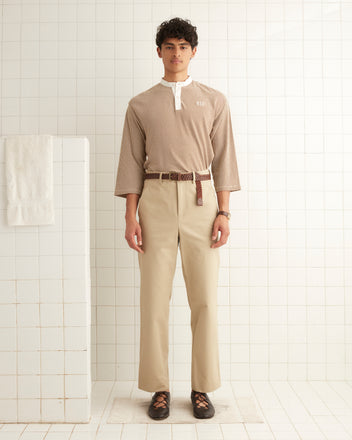 A man in Khaki Standard Trousers and a striped shirt stands in a tiled room with a white towel hanging on the wall.