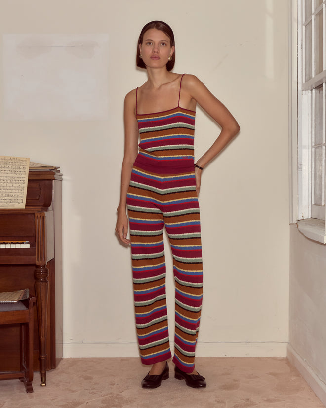 A woman in the Starkey Tank and a colorful striped jumpsuit stands by a piano in a softly lit room, sheet music resting on top.