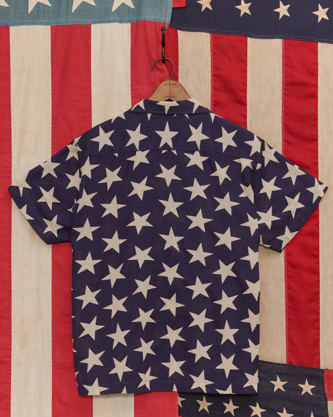 The Starry Short Sleeve Shirt features a vintage-inspired design with white stars on dark blue and bold red and white stripes, offering a standout look.