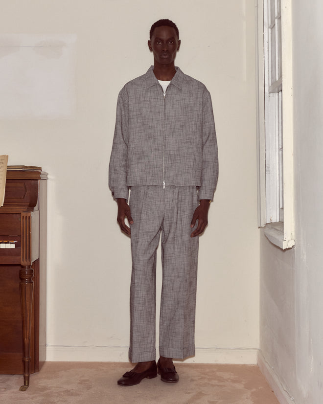 A man stands indoors by a piano and window wearing the Static Weave Ohio Jacket with matching pants, offering a modern twist on classic workwear style.
