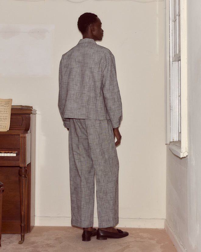 A person in the Static Weave Ohio Jacket stands facing a corner near a piano and window, offering a modern spin on classic suiting.
