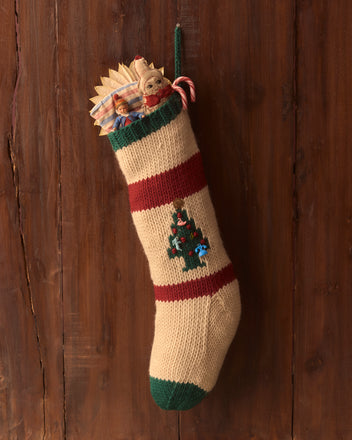 A Knit Holiday Stocking brimming with gifts and candy canes hangs charmingly on a rustic wooden wall, evoking memories of cozy Yule celebrations.