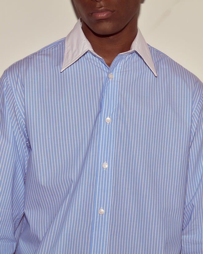A person wears a blue and white Striped Poplin Shirt featuring a crisp white collar; the photo is cropped below the nose.