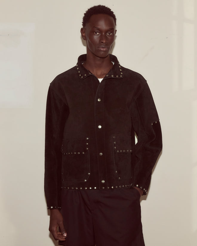 A person wearing a Studded Welding Jacket - Black stands against a plain light-colored wall.