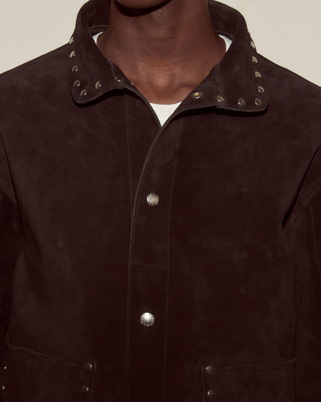A person is shown from the shoulders up wearing the Studded Welding Jacket - Black, featuring metal studs on the collar and snap buttons.